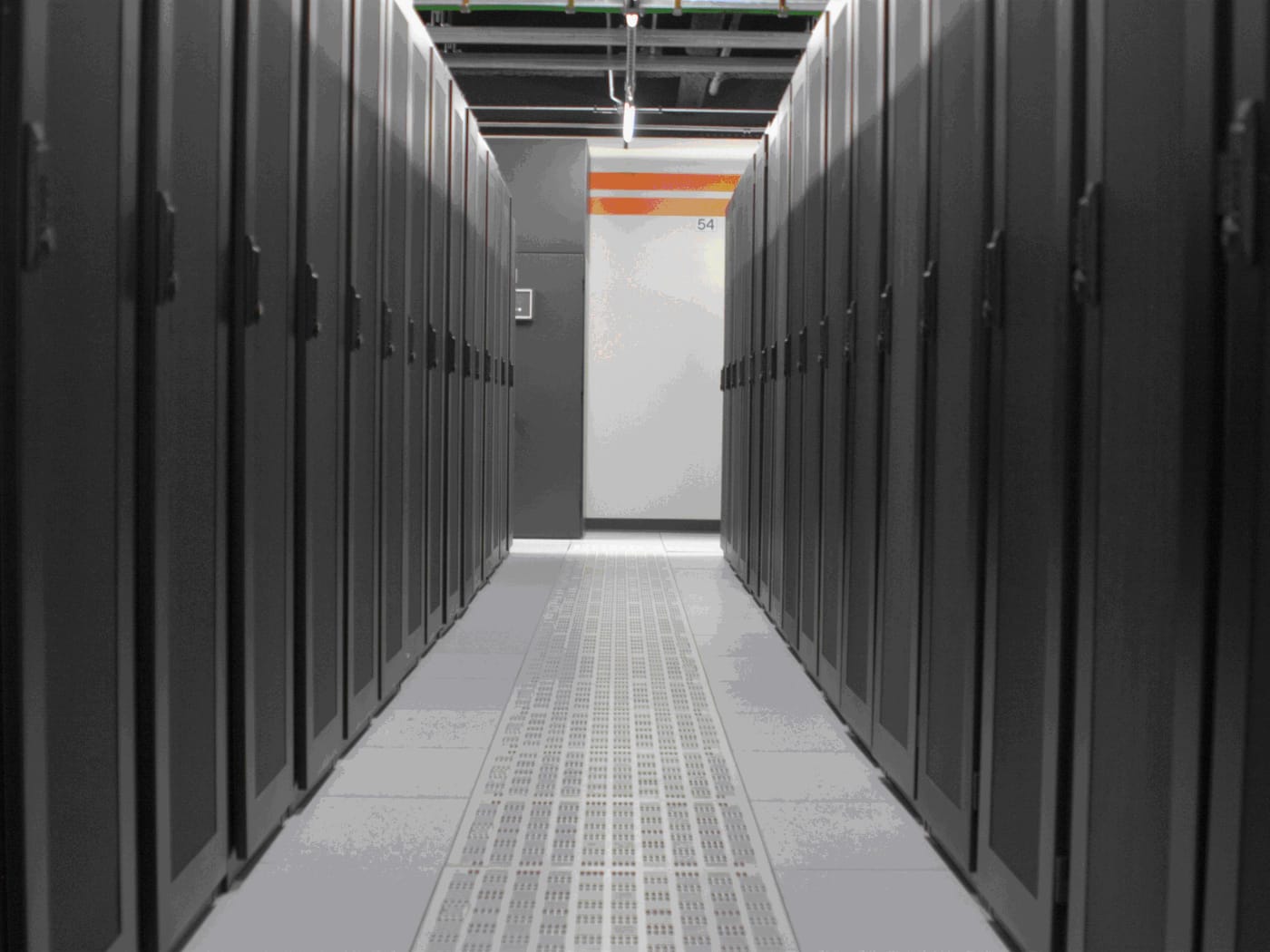 Corredor entre fileiras de racks escuros em um data center, com piso elevado perfurado